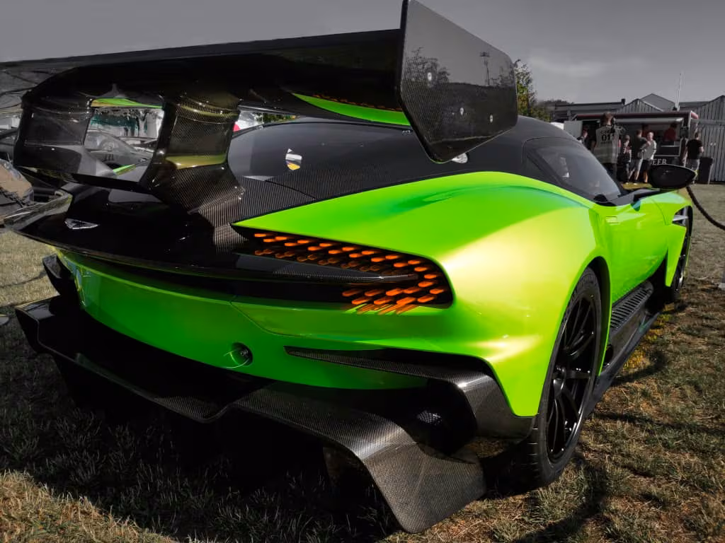 Skinnende grøn Aston Martin Vulcan sportsvogn med stor sort hækspoiler, set bagfra, parkeret på en græsplæne.