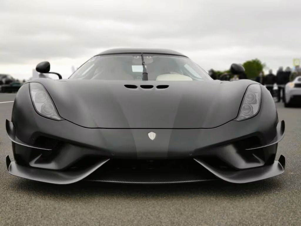 Mattsort Koenigssegg regera sportsvogn set forfra på en grå dag.