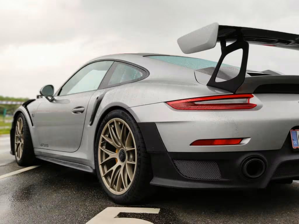 Sølvfarvet Porsche 911 GT2 RS set skråt bagfra med stor bagspoiler og sorte detaljer på en parkeringsplads.